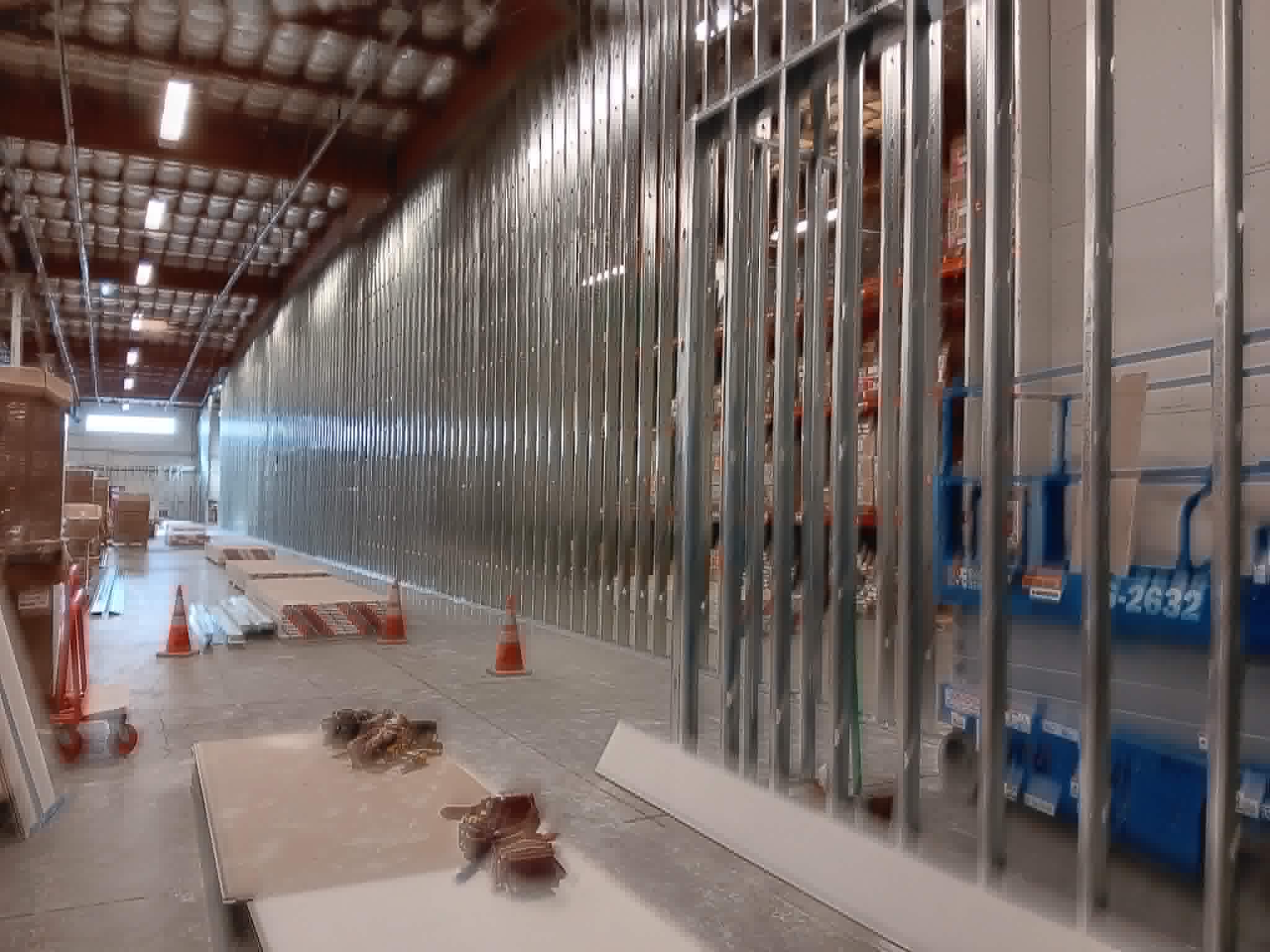 Metal stud framing in a large commercial warehouse — tall steel studs forming a new partition wall with warehouse shelving visible beyond